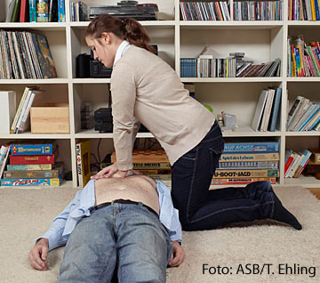 Frau kniet vor bewusstlosem Mann und macht eine Herzmassage.