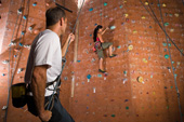 In der Kletterhalle: Ein Mann sichert eine Frau, die an der Kletterwand klettert.