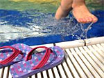 Ein Kind steigt aus dem Schwimmbad. Am Rand liegen Badelatschen.