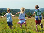 Drei Kinder halten sich an den H�nden und laufen �ber eine Wiese.
