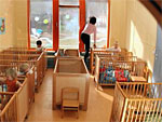 Man sieht mehrere Kinder in Kinderbetten in einer Kita und eine Betreuerin.