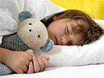 Man sieht ein schlafendes Kind mit einem Teddybär im Arm.