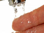Man sieht zwei Finger unter einem laufenden Wasserhahn.