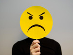 Das Bild zeigt eine Person, die ein Schild mit einem traurigen Smiley vor ihr Gesicht h�lt. 