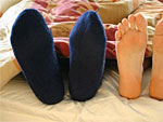 Man sieht zwei paar F��e unter einer Bettdecke hervorschauen: eins mit Socken und eins ohne.
