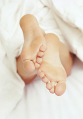 Frauenf��e ragen unter einer wei�en Bettdecke hervor.