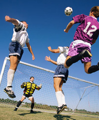 Auf dem Foto sind drei Fu�ballspieler zu sehen, die gemeinsam zum Kopfball hochsteigen. Im Hintergrund ist der Torwart zu sehen.