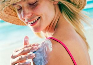 Frau am Strand schmiert sich mit Sonnencreme an der Schulter ein