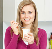 Eine blonde Frau isst ein Joghurt.