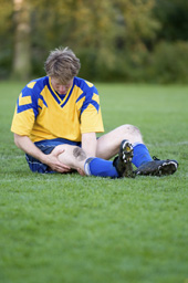 Das Bild zeigt einen verletzten Fu�ballspieler, der am Boden liegt und sein Bein h�lt