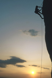 Ein Kletterer an einer steilen Wand mit einem Abendhimmel-Panorama im Hintergrund.