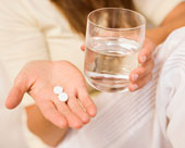 Frau h�lt Tabletten in einer, ein Glas Wasser in der anderen Hand.