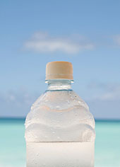 Eine Flasche Wasser, im Hintergrund ein Strand.