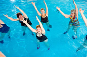�ltere Frauen stehen in einem Schwimmbecken und strecken ihre Arme Richtung Decke