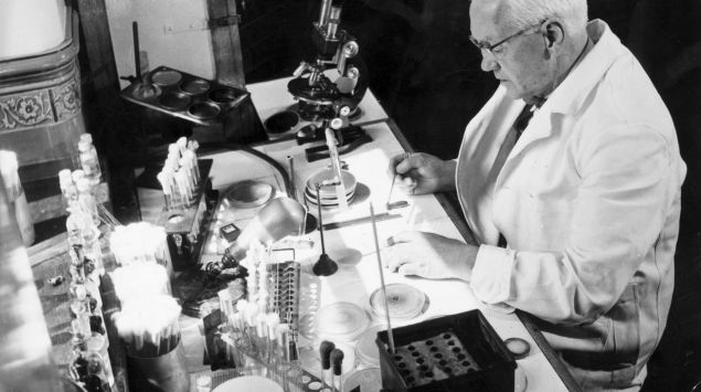 Foto aus dem Jahr 1954 von Sir Alexander Fleming, der in einem Labor an einem Tisch sitzt.