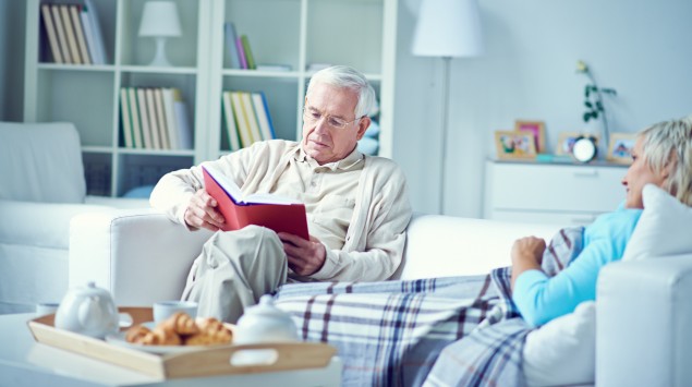 Ein älterer Mann sitzt mit seiner Frau auf dem Sofa und liest.