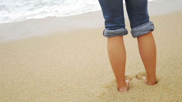 Eine Person steht barfuß am Strand.