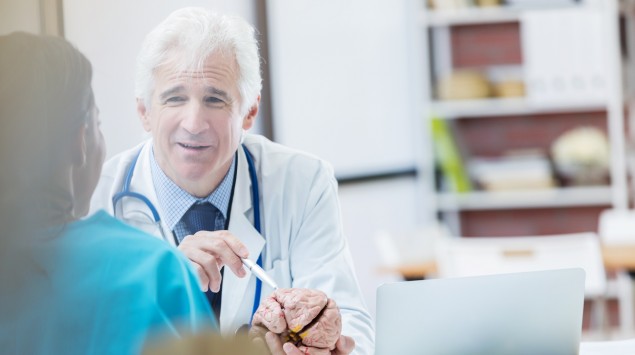 Ein Arzt erklärt etwas einer Patientin, er hat ein Gehirnmodell in der Hand.