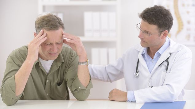 Ein Arzt tröstet einen Patienten, der sich die Hände an den Kopf hält