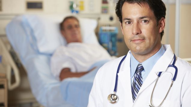Das Bild zeigt im Vordergrund einen Arzt und im Hintergrund einen Patienten.