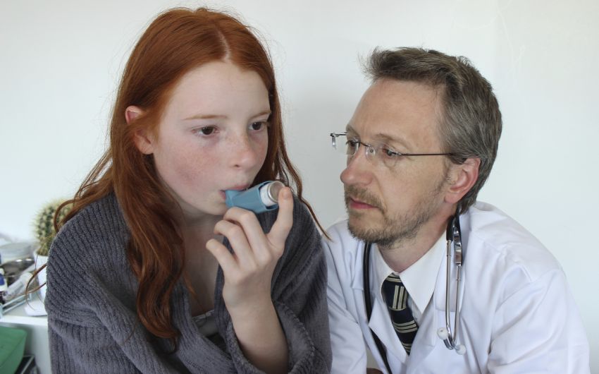 Das Bild zeigt ein junges Mädchen, das unter Anleitung eines Arztes ein Asthmaspray benutzt.