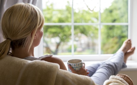 Burnout-Syndrom: Eine Frau sitzt im Sessel, hält eine Tasse in den Händen und schaut aus dem Fenster.