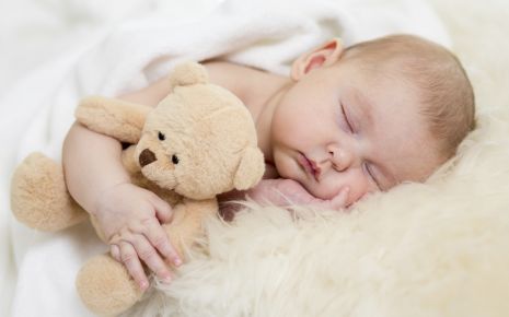 Ein Baby schläft, im Arm hält es einen Teddy
