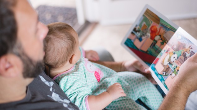 Das Bild zeigt einen Vater, der mit seinem Baby ein Bilderbuch ansieht.