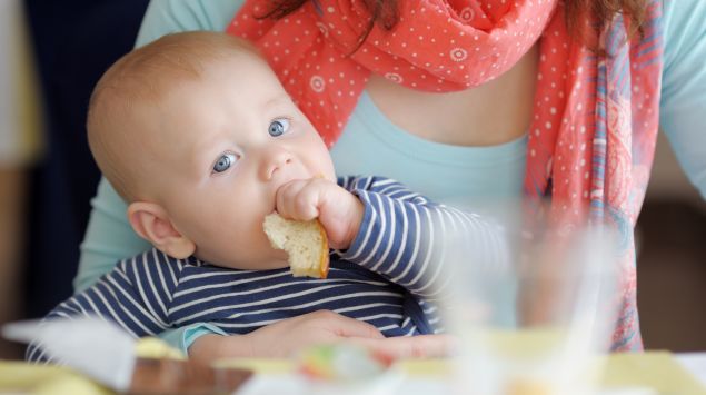 Das Bild zeigt ein Baby, das ein Stück Brot isst.