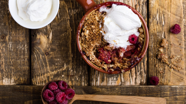 Baked Oatmeal mit Himbeeren und Joghurt auf einem braunen Holztisch