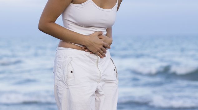 Das Bild zeigt eine Frau am Strand, die sich den Bauch hält.