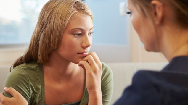 Eine junge, bedrückt aussehende Frau wird von einer anderen Frau getröstet.