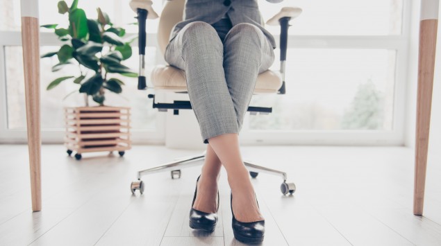 Man sieht die Beine einer Frau, die auf einem Bürostuhl sitzt.