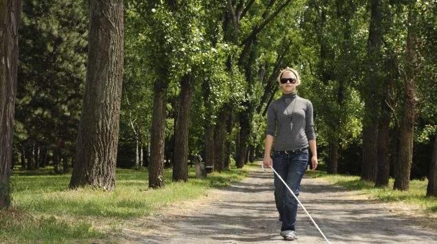 Eine blinde Frau läuft auf einem Parkweg.