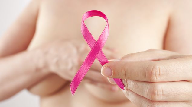 Eine Frau verdeckt ihre Brüste und hält eine pinke Brustkrebsschleife in der Hand.