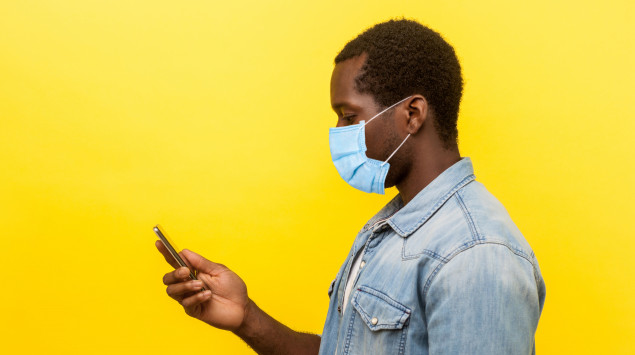Ein Mann mit Maske schaut auf sein Smartphone