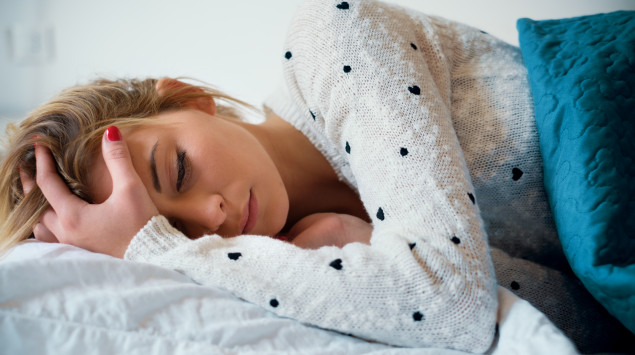 Ein Mädchen liegt im Bett und hält sich den Kopf
