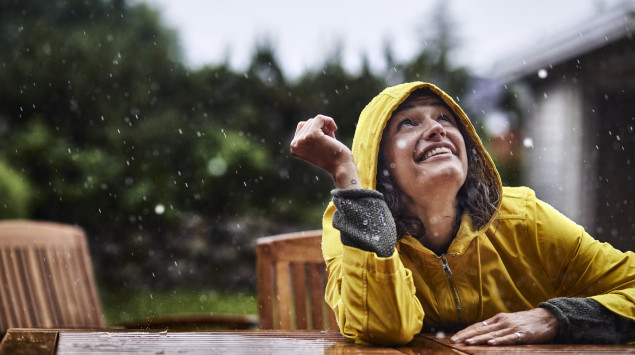 eine Frau mit Regenjacke sitzt im Regen und lacht: Nach überstandener Infektion ist man immun gegen das Coronavirus