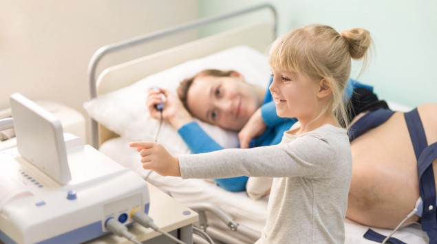 Das Bild zeigt eine Frau mit ihrer Tochter, die an ein Gerät zur Messung der CTG-Werte angeschlossen ist.