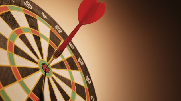 Das Bild zeigt eine Dartscheibe, in der ein Pfeil in der Mitte steckt.