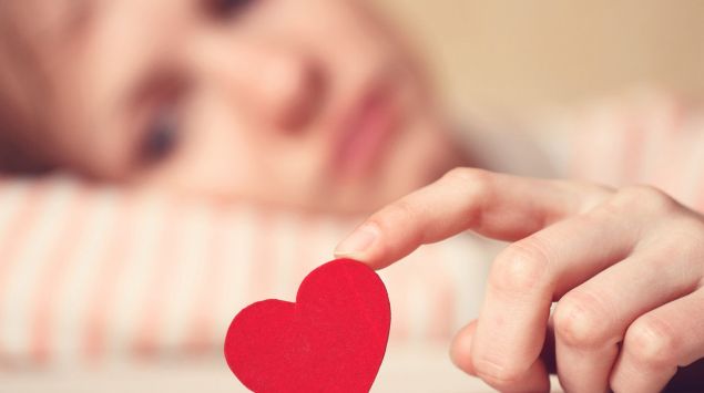 Eine traurig aussehende Frau hält ein rotes Herz in der Hand.