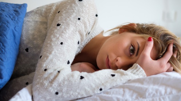 Junge Frau liegt unglücklich im Bett.