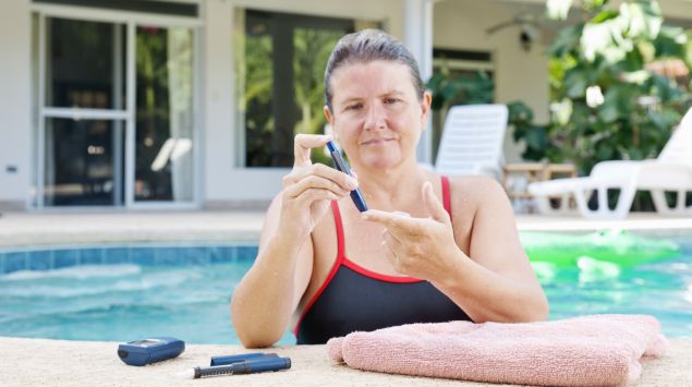 Das Bild zeigt eine Frau im Pool, die ihren Blutzucker misst.