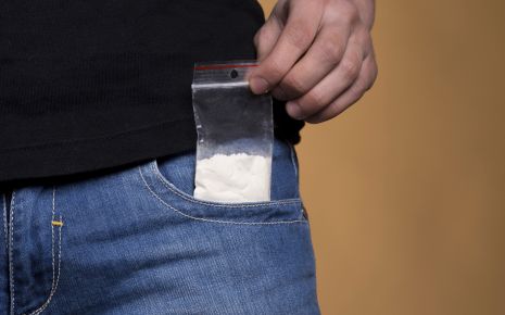 Jemand zieht ein Tütchen mit einem weißen Pulver aus der Hosentasche.