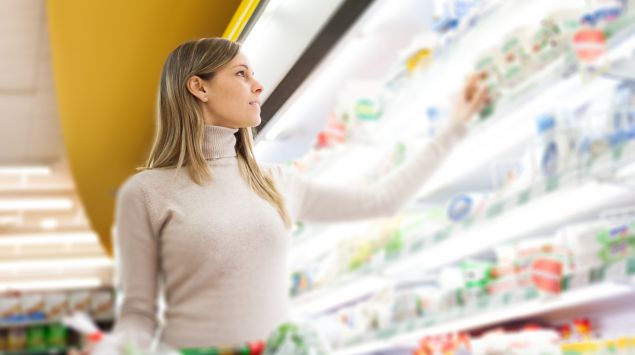 Eine Frau steht vor einem Kühlregal im Supermarkt.
