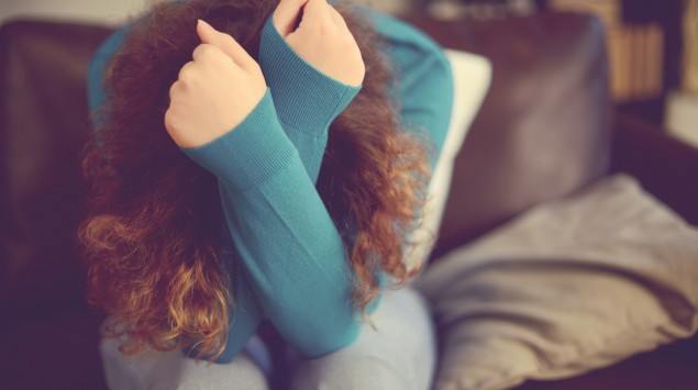 Ein Frau sitzt auf einem Sofa und hat ihren Kopf in den Armen vergraben.