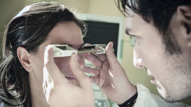 Eine Augenarzt untersucht die Augen einer Frau mit einem Exophthalmometer.
