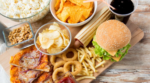 Man sieht ein Holzbrett mit verschiedenen Fast Food-Gerichten und Snacks sowie einen Becher Cola.