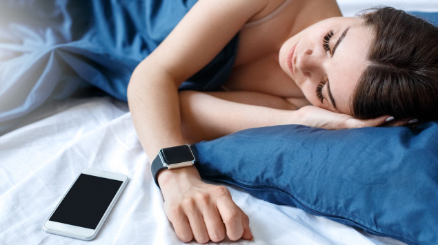 Eine Frau schläft neben ihrem Handy und trägt eine Smartwatch