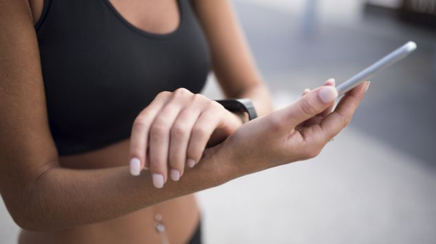 Das Bild zeigt eine sportliche Frau mit einer Smartwatch und einem Smartphone.